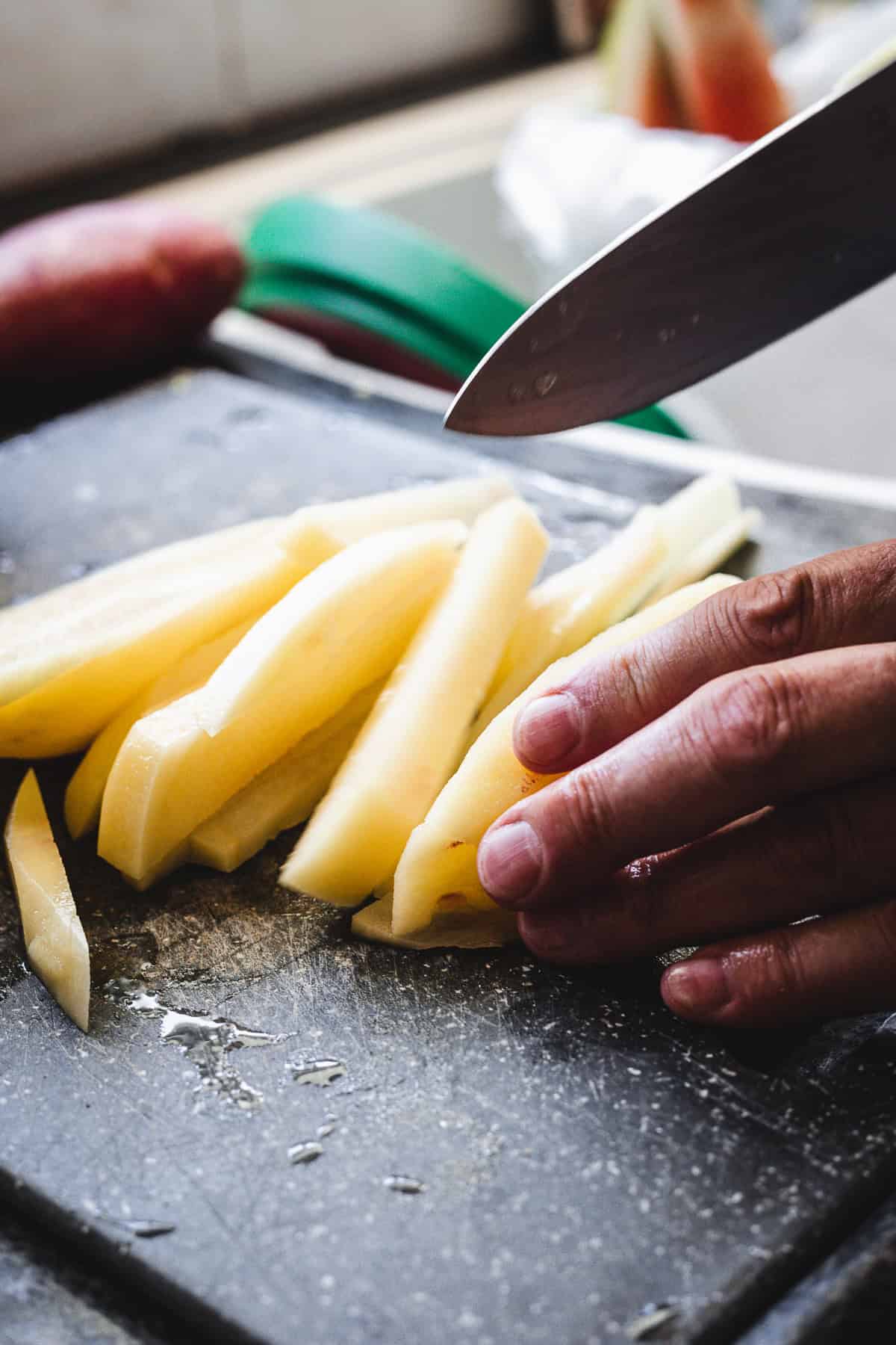 Hand slicing potatoes into thin strips on a cutting board with a knife, perfect for making authentic Russian Fried Potatoes.