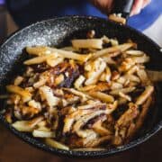 A hand holds a pan filled with crispy, golden-brown fried potatoes.