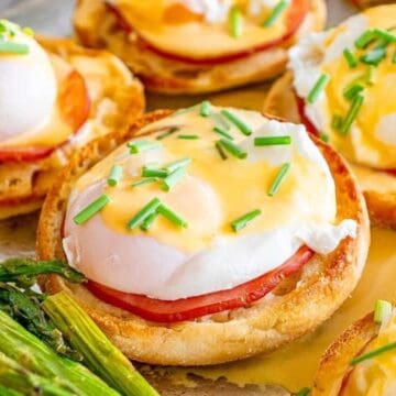 A classic breakfast favorite: Eggs Benedict with ham and hollandaise sauce on English muffins, garnished with chives and served with asparagus.