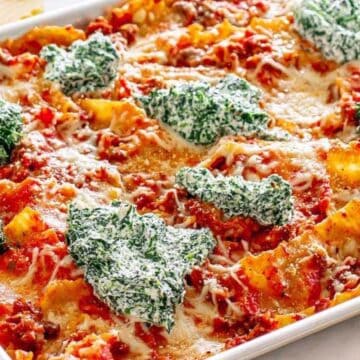 A baked lasagna in a pan topped with spinach and ricotta cheese mixture, with melted cheese and tomato sauce.