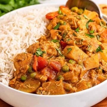 A bowl of rice and vegetable curry with peas and potatoes, garnished with herbs, and a spoon on the side.