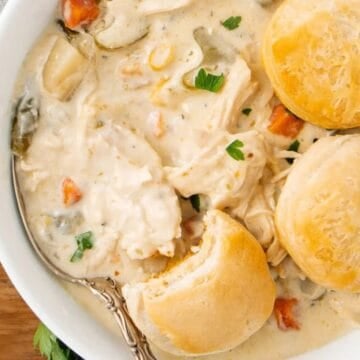 Bowl of creamy chicken and vegetable stew topped with three biscuits and garnished with parsley.