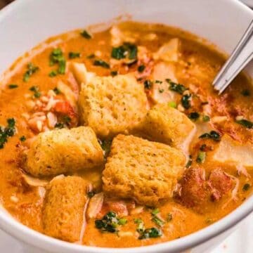 A bowl of creamy soup topped with croutons and herbs, with a spoon resting inside.