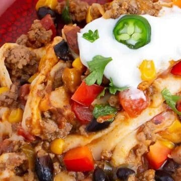 A colorful plate of taco casserole topped with sour cream, jalapeño, chopped tomatoes, and cilantro.