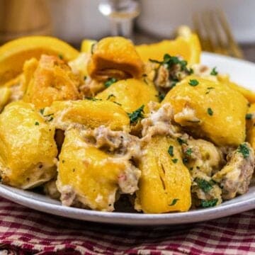 A plate of crispy roasted potatoes topped with creamy sauce and herbs, on a red checkered napkin.