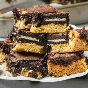 A stack of layered cookie and brownie bars with Oreo cookies inside, displayed on parchment paper.