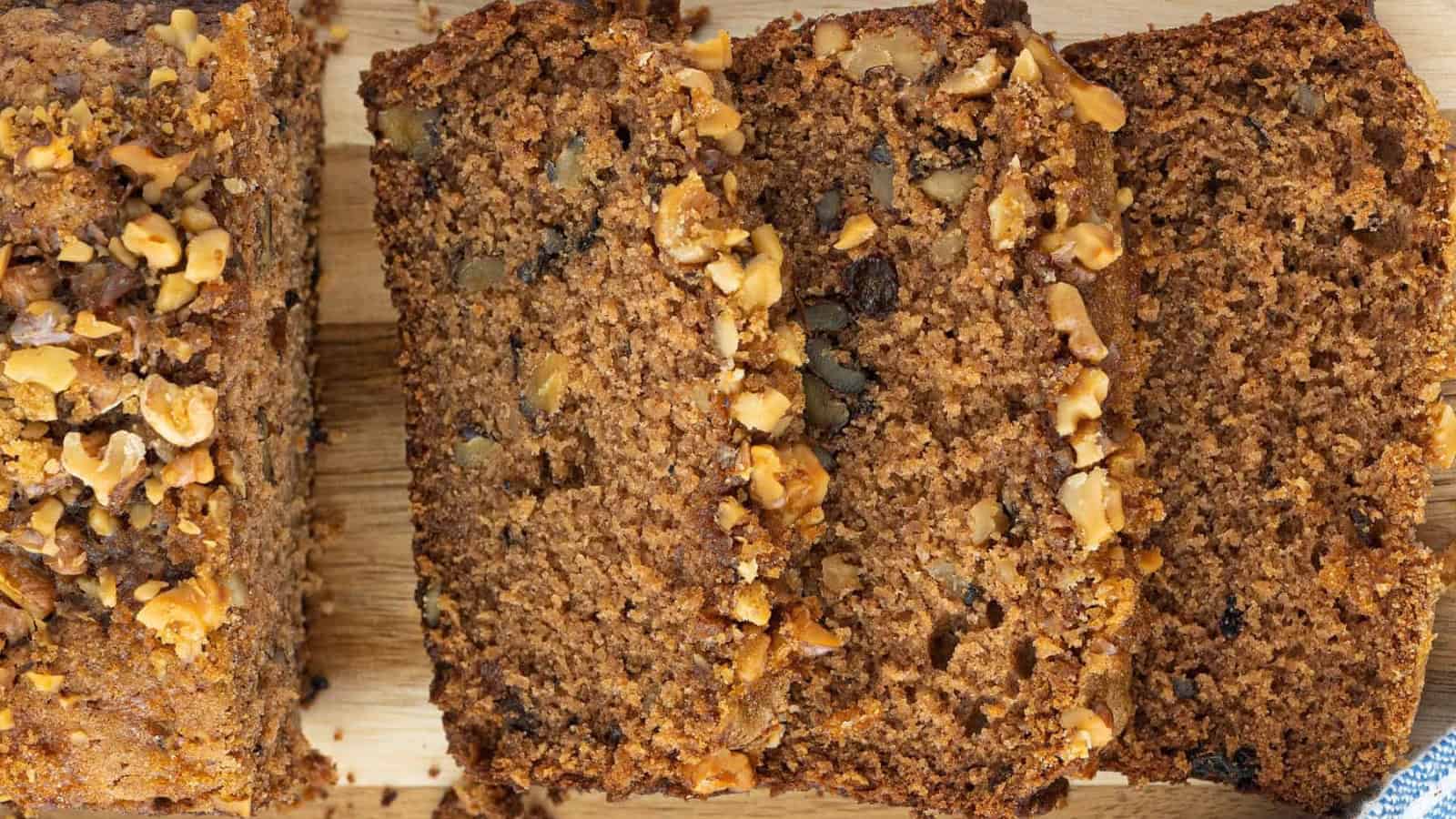 Four slices of nut-topped banana bread on a wooden surface, shown from above.