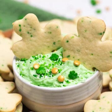 Shamrock-shaped cookies surround a bowl of green dip topped with sprinkles.