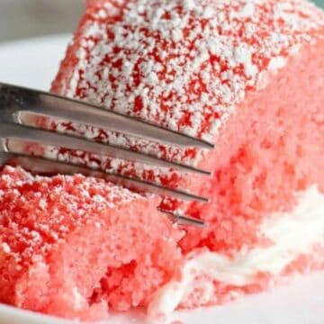 A fork cutting into a slice of pink cake with white frosting and powdered sugar on top.
