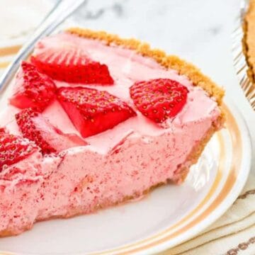 A slice of strawberry cream pie with fresh strawberries on a plate, next to the rest of the pie.
