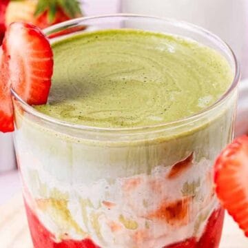 A layered strawberry and matcha dessert in a glass, garnished with a sliced strawberry on the rim.