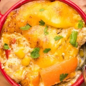 Cheesy casserole with carrots, corn, and herbs in a red dish, served with a spoon.
