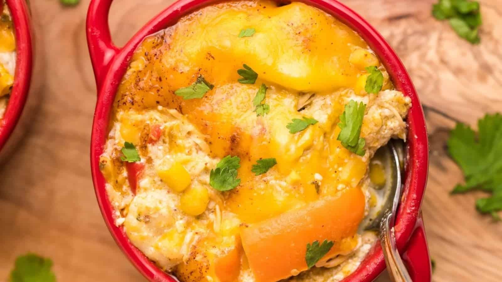 Cheesy casserole with carrots, corn, and herbs in a red dish, served with a spoon.
