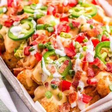 Loaded tater tots topped with cheese, jalapeños, bacon, tomatoes, green onions, and a drizzle of sauce.
