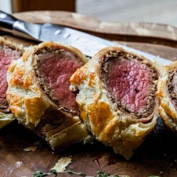 Four slices of beef Wellington on a wooden board with a knife in the background.