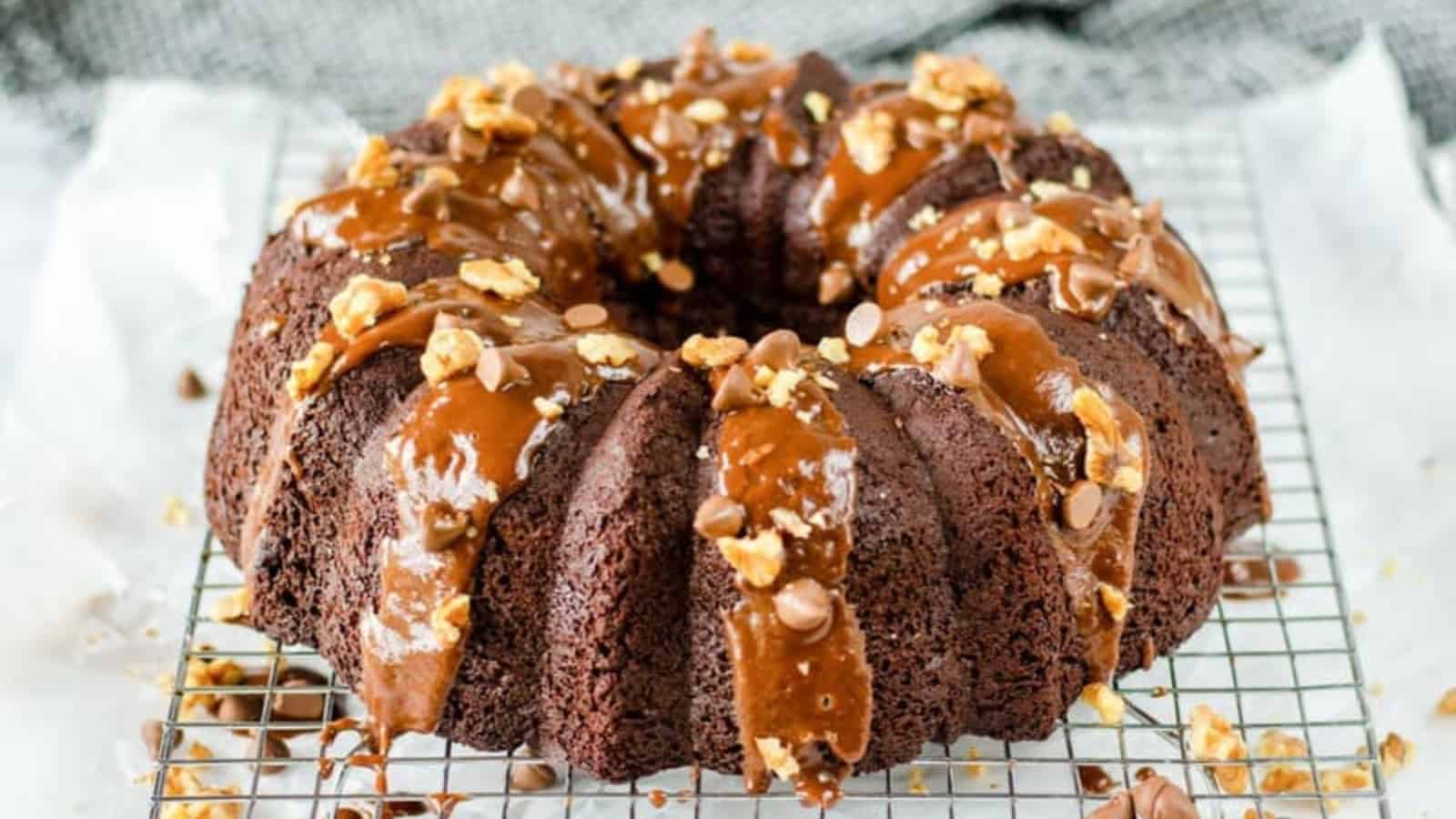 Chocolate bundt cake with caramel glaze, nuts, and chocolate chips on a cooling rack.