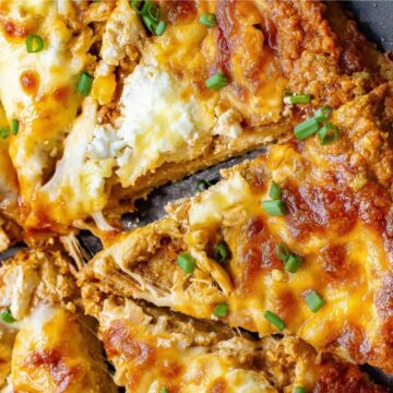 Close-up of a cheesy pizza with shredded chicken and chopped green onions, sliced in a pan.