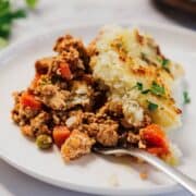 A serving of shepherd’s pie with ground meat, vegetables, and mashed potato crust on a white plate.