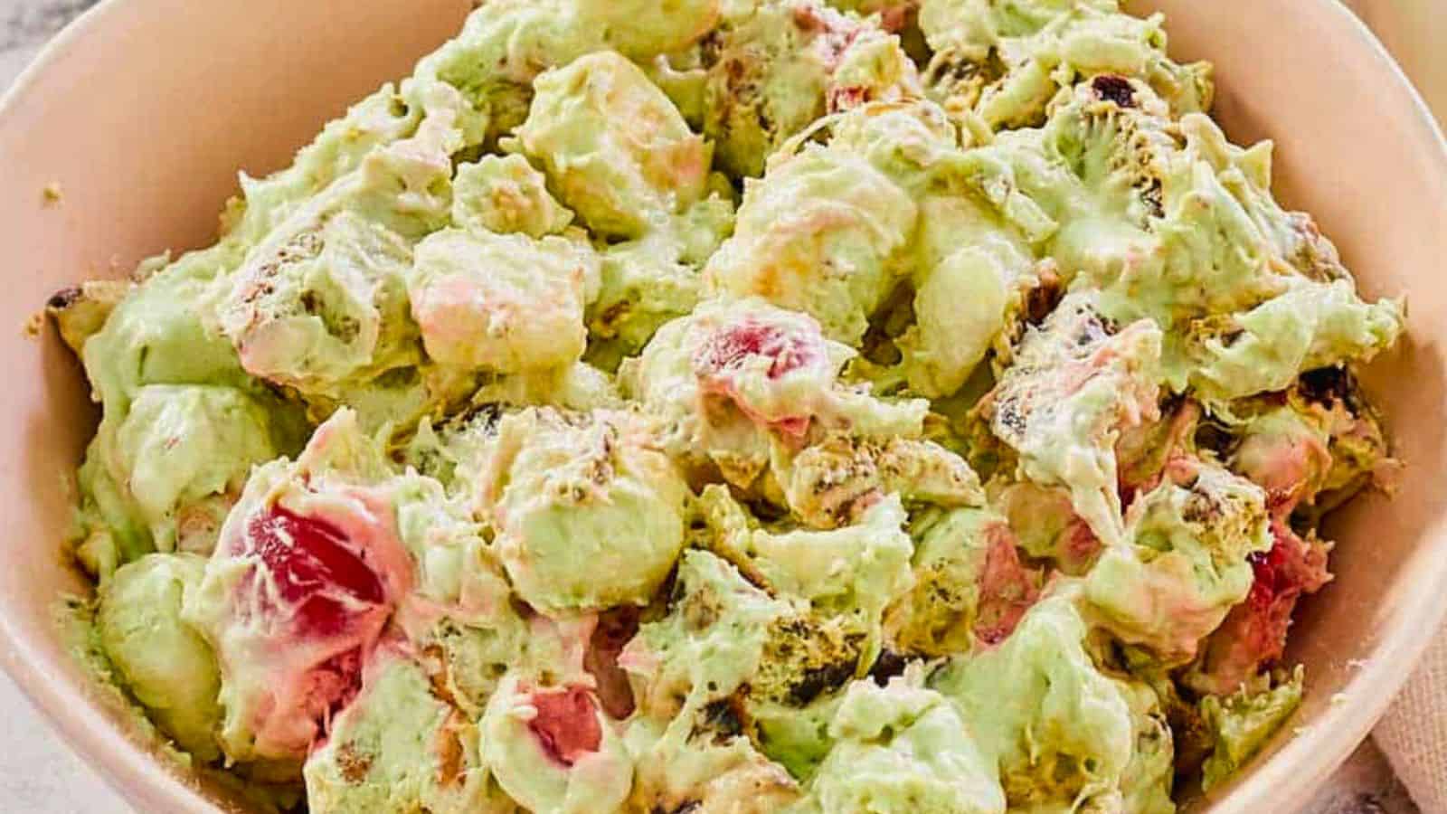 A bowl of green-tinted fruit salad mixed with marshmallows and creamy dressing.