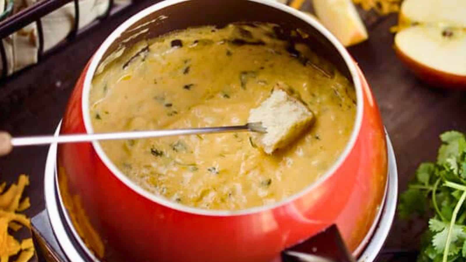 A piece of bread is dipped into a pot of melted cheese fondue with herbs.