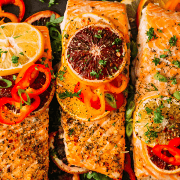 Baked salmon fillets topped with lemon, blood orange slices, red peppers, and fresh herbs.