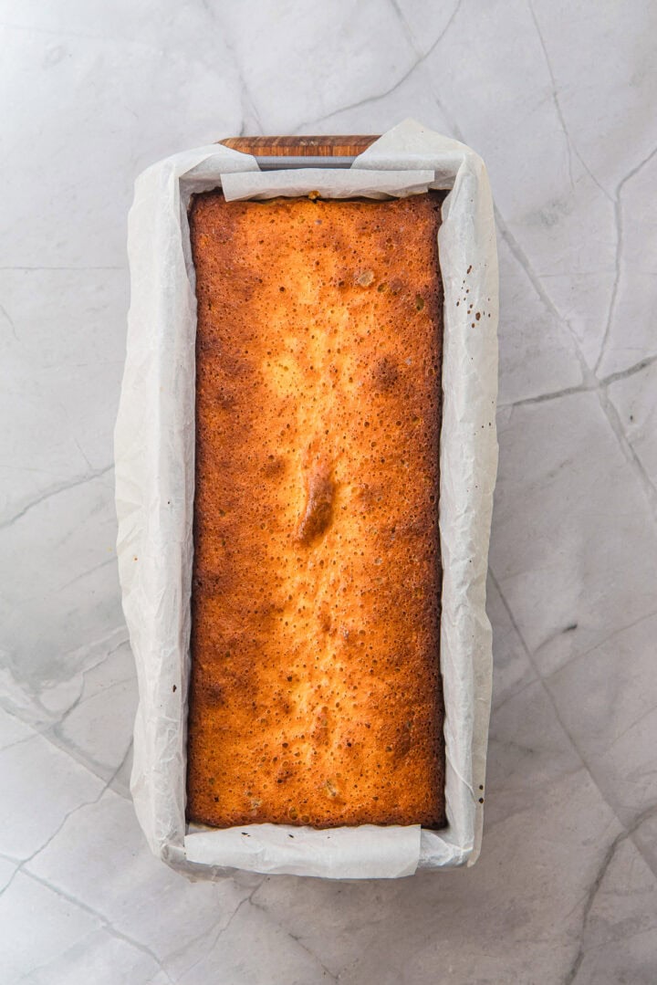 A golden-brown rectangular loaf cake in a parchment-lined baking tin on a marble surface.