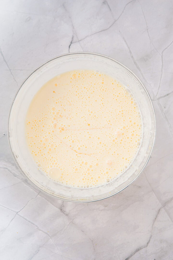A glass bowl filled with light yellow, frothy batter on a marble countertop.