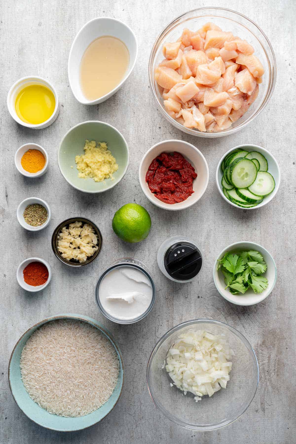 Overhead view of ingredients in bowls, including diced chicken, rice, spices, lime, cucumber, and herbs—perfect for assembling fresh Coconut Chicken Rice Bowls.