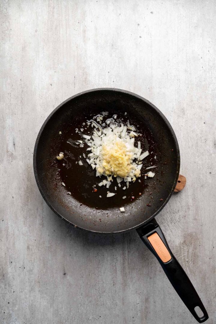 A frying pan with chopped onions and minced garlic cooking in oil on a light, textured surface—perfect beginnings for flavorful Coconut Chicken Rice Bowls.