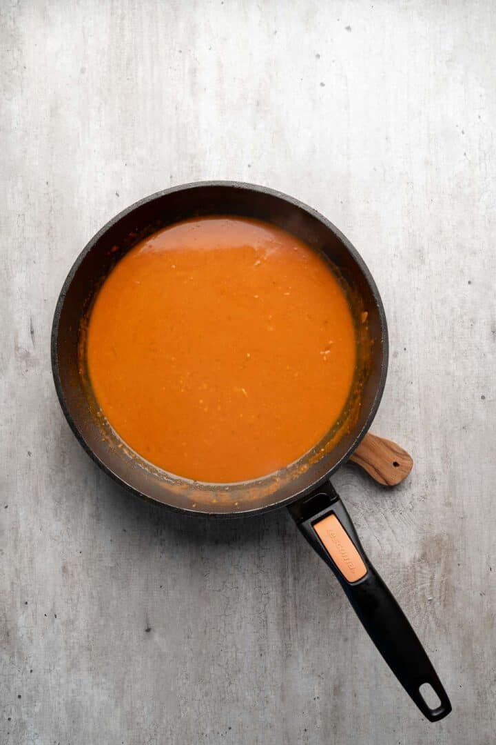 A black frying pan filled with smooth orange sauce on a light gray surface, perfect for drizzling over Coconut Chicken Rice Bowls.