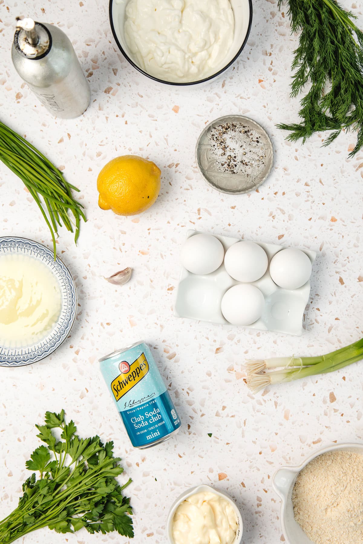 Eggs, herbs, lemon, seasoning, and dairy products arranged on a white speckled countertop.