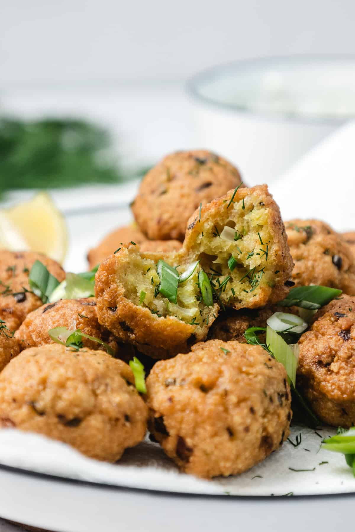 A plate of crispy falafel balls, one split open to show the green, herby filling inside.