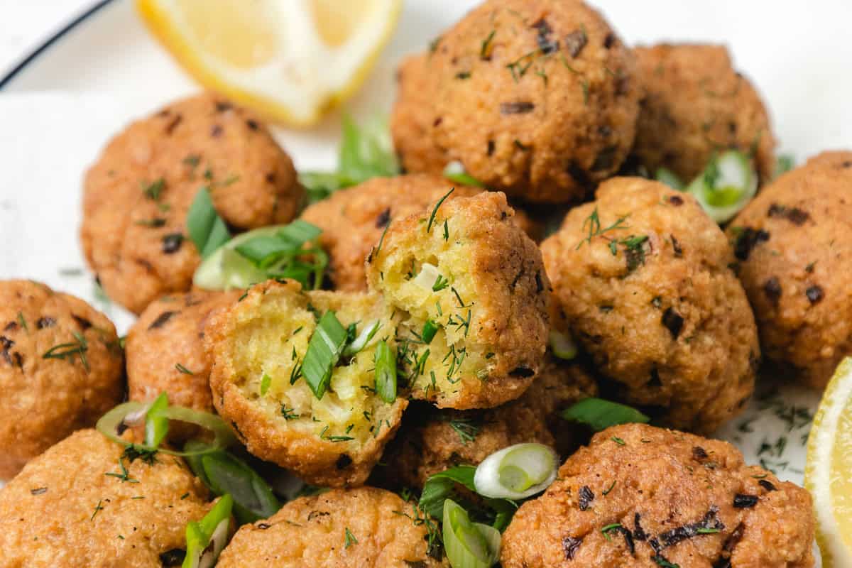 A close-up of crispy falafel balls, one split open, garnished with fresh herbs and served with lemon wedges.
