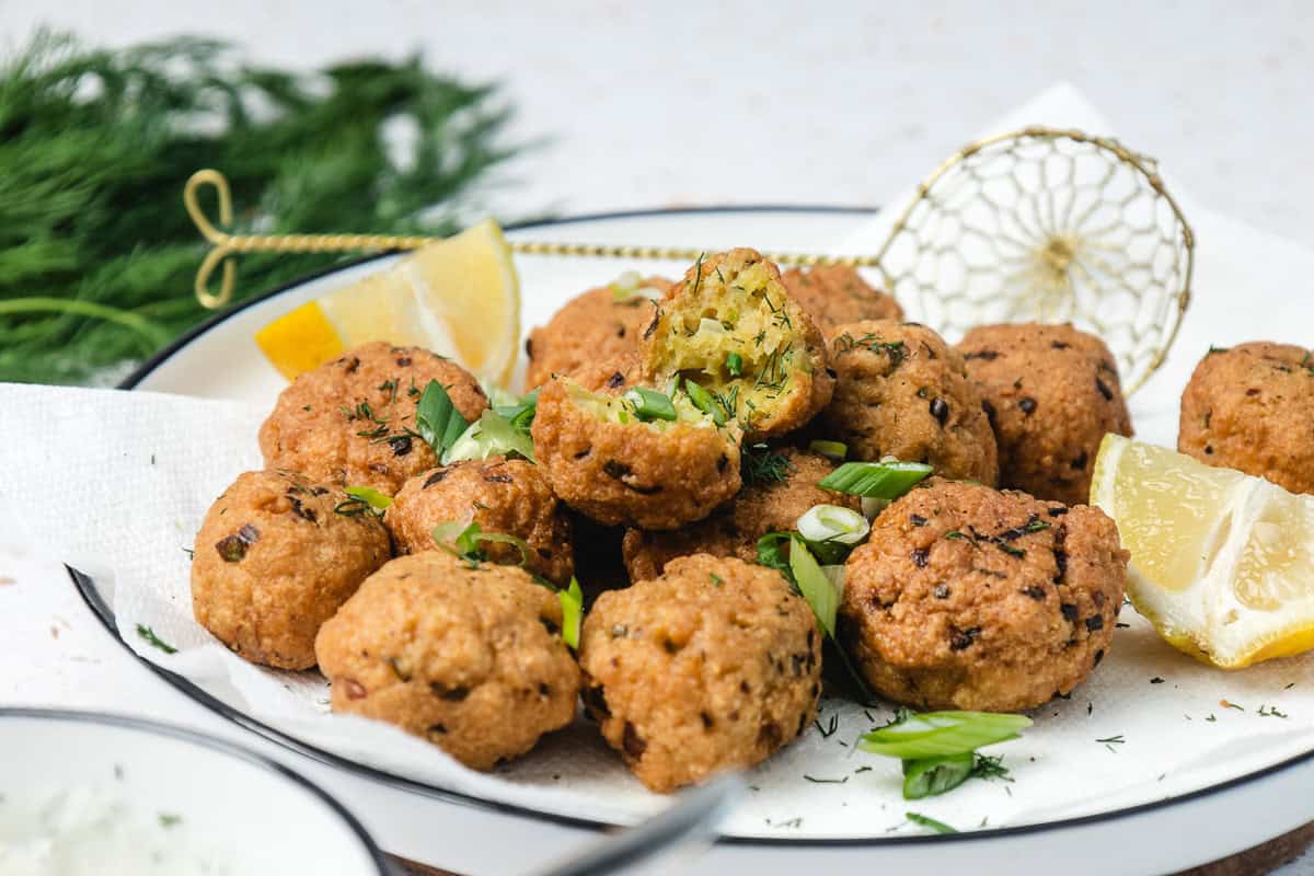 A plate of golden falafel balls garnished with green herbs and lemon wedges on a paper towel.
