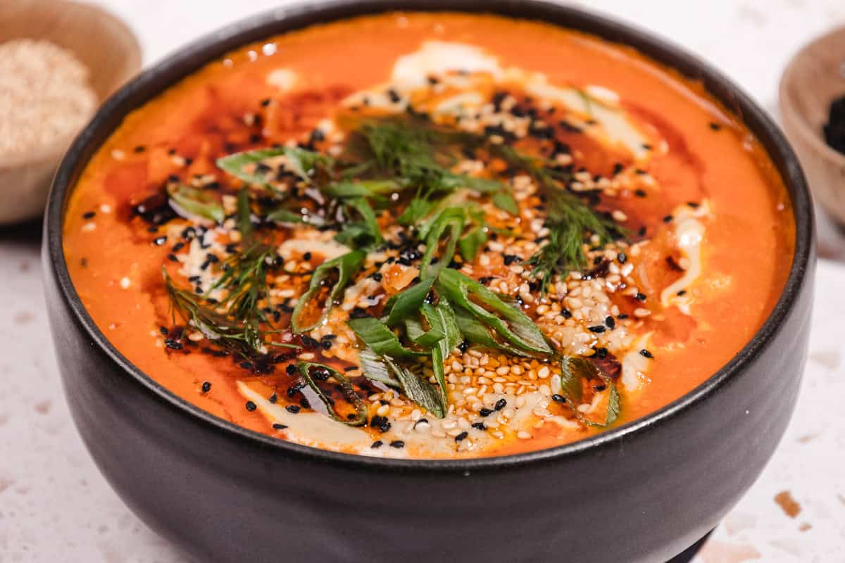 A bowl of creamy tomato soup topped with sesame seeds, herbs, and sliced green onions, inspired by the bold flavors of Gochujang Tahini Cabbage Soup.