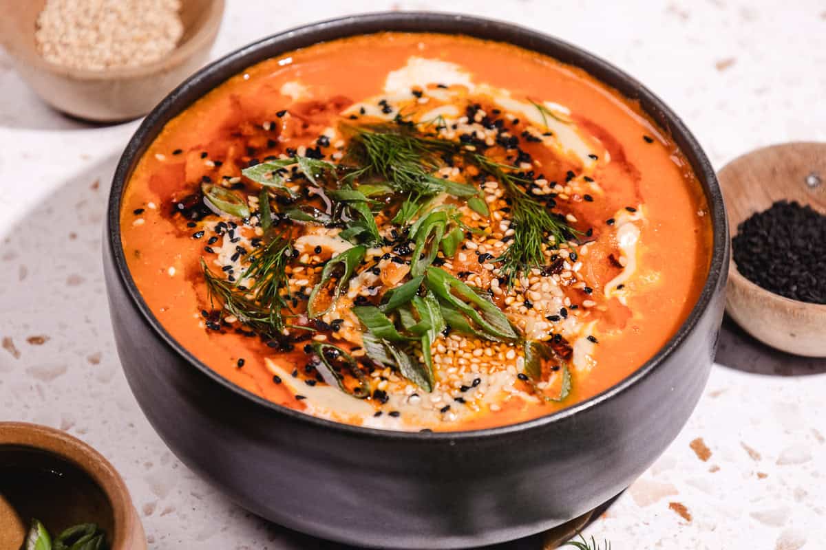 A bowl of Gochujang Tahini Cabbage Soup topped with herbs, sesame seeds, black seeds, and a swirl of cream.
