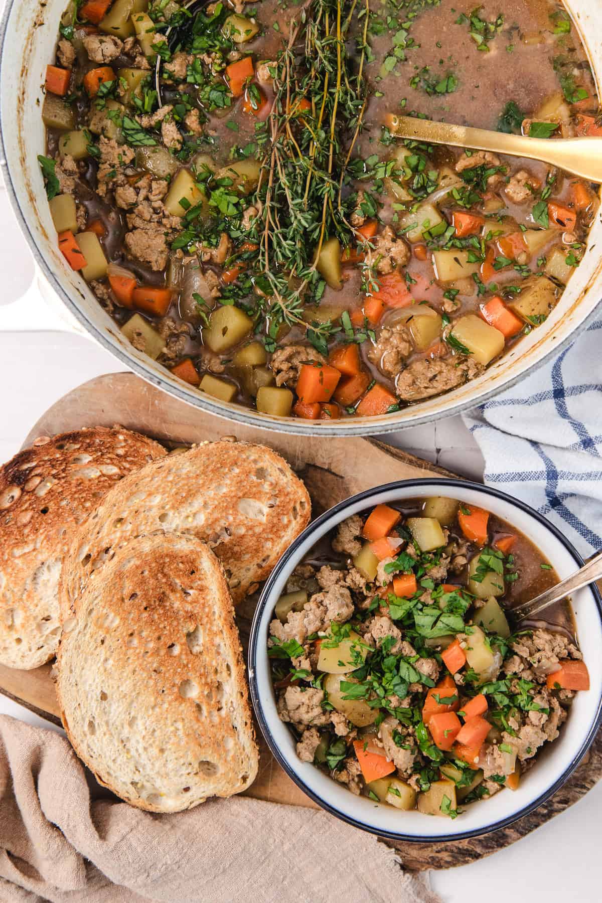 A bowl and pot of vegetable and ground meat soup with herbs, served with slices of toasted bread on the side.