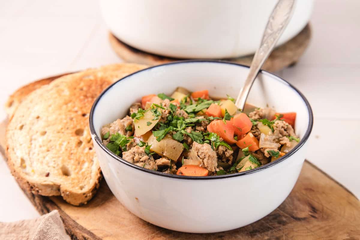 A bowl of Irish Ground Turkey and Vegetable Stew with herbs, served alongside two slices of toasted bread.