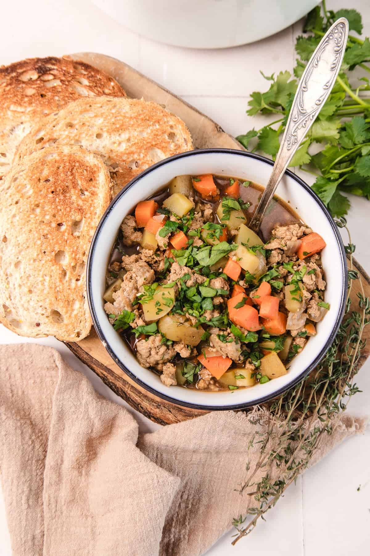 A bowl of hearty vegetable and ground meat soup, garnished with herbs, served with toasted bread on the side.