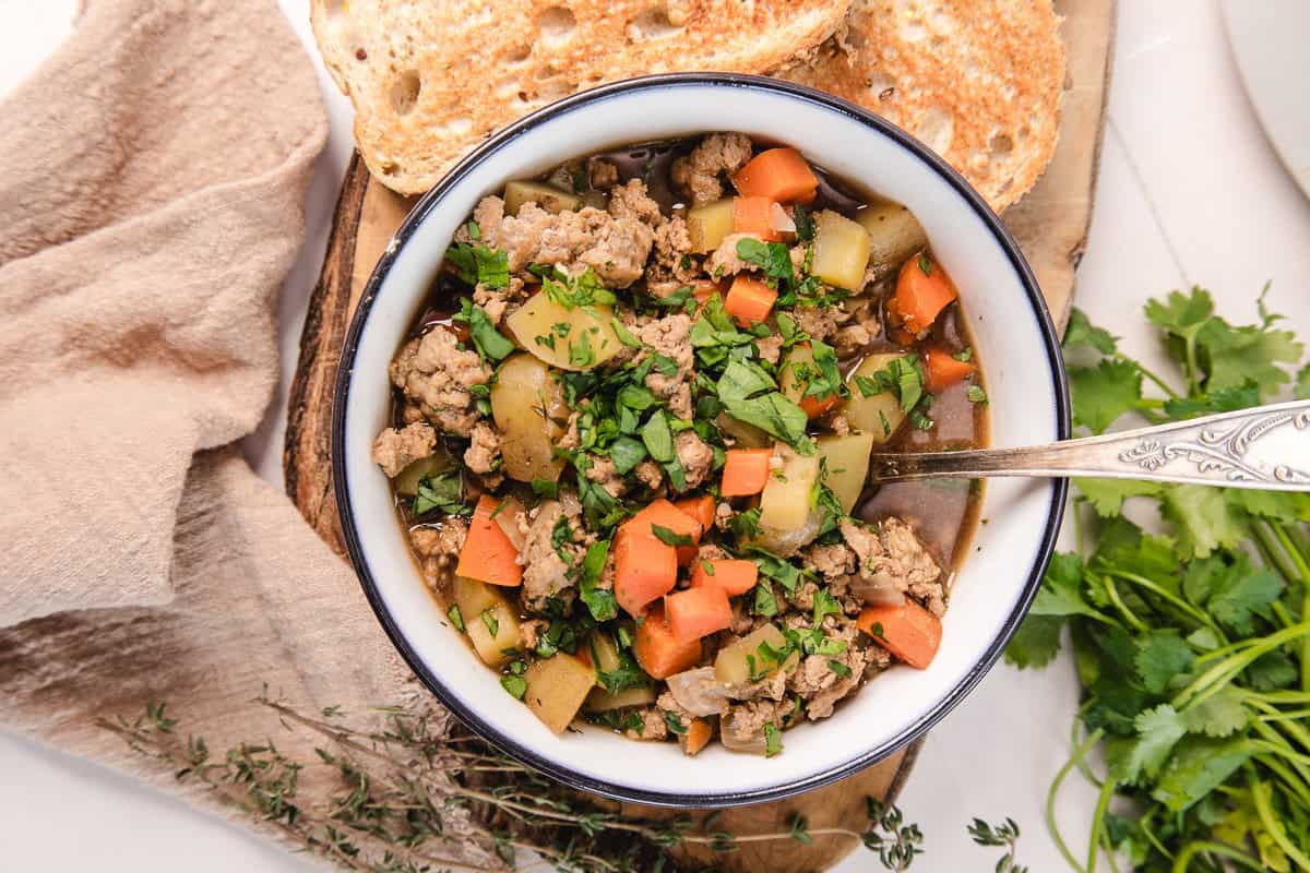 A bowl of hearty vegetable and ground meat stew with herbs, served with toasted bread on the side.