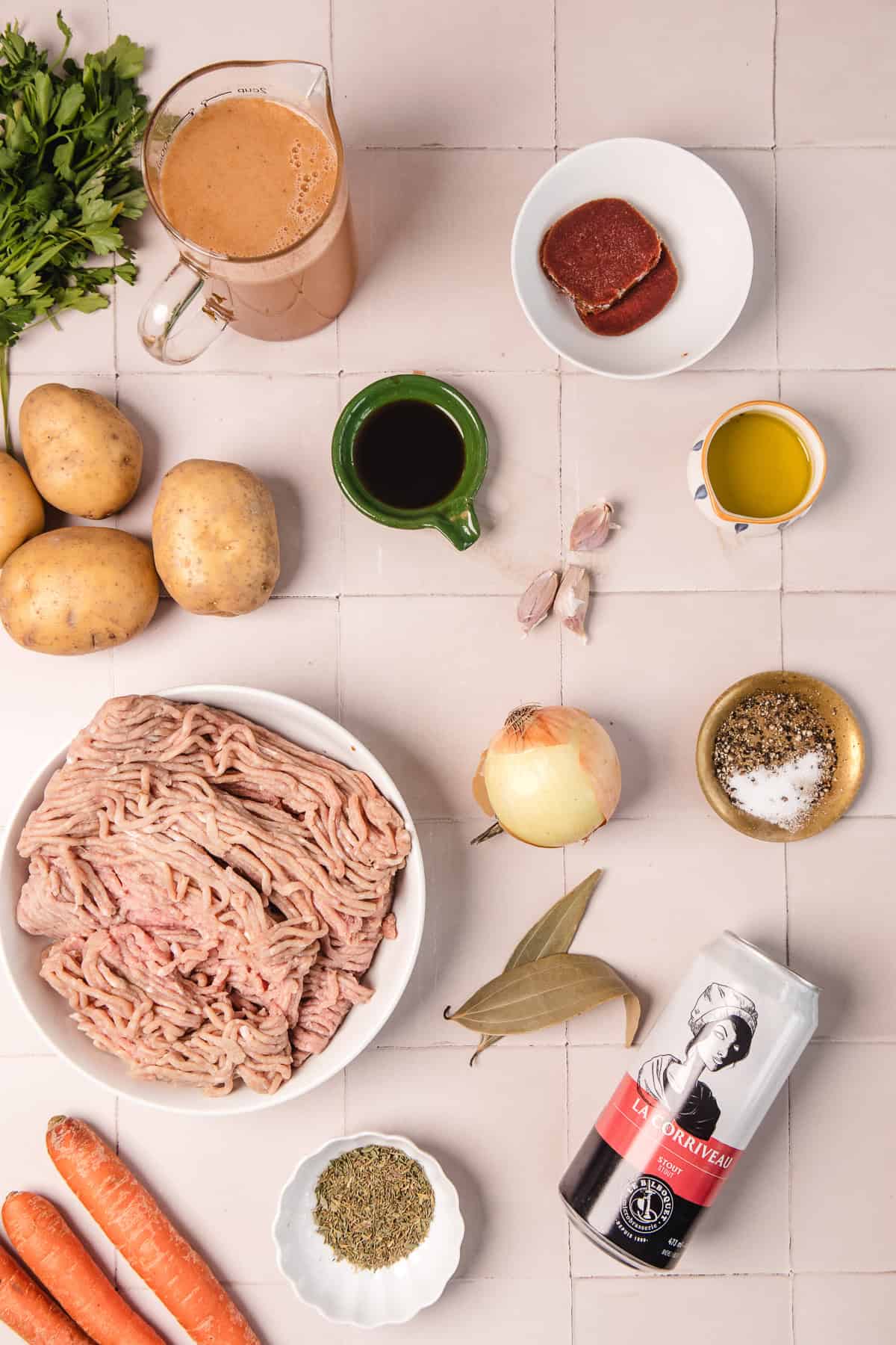 Ingredients for a beef stew, including ground meat, potatoes, carrots, onion, herbs, broth, oil, and tomato paste.