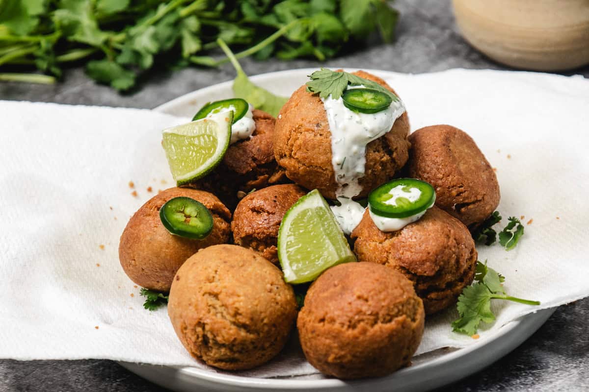 Plate of falafel balls garnished with lime wedges, jalapeño slices, cilantro, and a drizzle of creamy sauce.