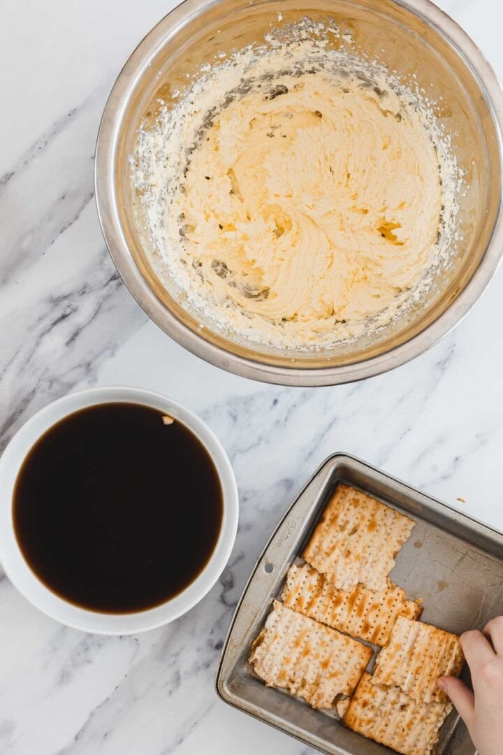 A bowl of creamy mixture, a cup of coffee, and a pan with crackers on a marble surface.