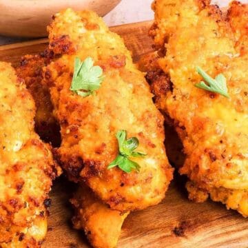 Golden, crispy chicken tenders garnished with fresh parsley on a wooden board.