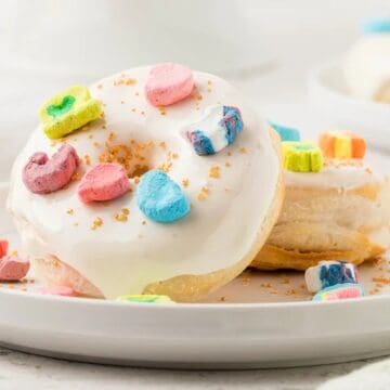 A white-frosted donut topped with colorful marshmallow cereal pieces on a white plate.