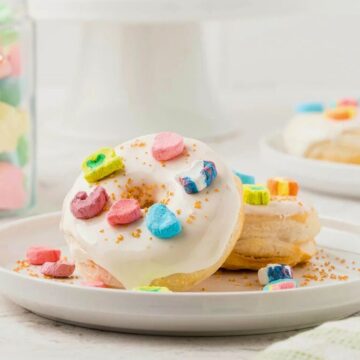 Iced biscuits topped with colorful marshmallow cereal on a white plate, with a jar of cereal in the background.