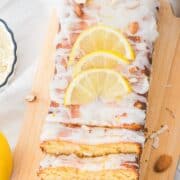 Lemon loaf cake with icing, sliced almonds, and lemon slices on top, on a wooden board.