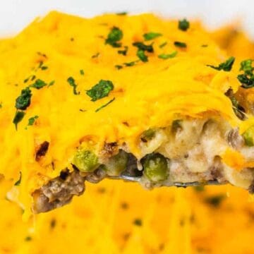 A spoonful of cheesy casserole with peas, ground beef, and a golden melted cheese topping.