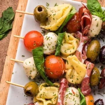 Colorful skewers with tortellini, olives, mozzarella, tomatoes, basil, and cured meat make perfect graduation party appetizers on a white plate.