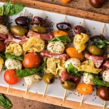 Skewers with mozzarella, tomatoes, tortellini, olives, basil, and cured meat on a white plate—perfect graduation party appetizers for your celebration.